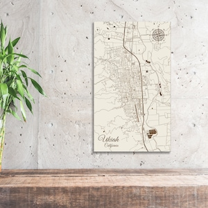 May include: A wooden map of Ukiah, California, with brown lines and text. The map is on a light beige background and has a compass rose in the top right corner.