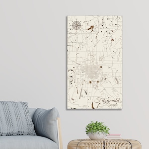 May include: A wooden map of Fitzgerald, Georgia, with a compass rose in the top left corner. The map is laser cut and shows the city's streets and landmarks. The city name is written in a decorative font at the bottom of the map.