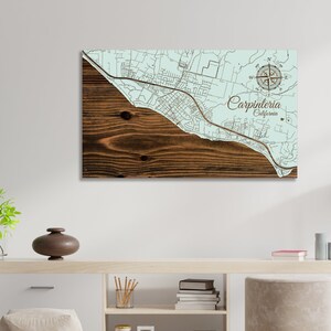 May include: A wooden map of Carpinteria, California, with a compass rose and a light blue background. The map is mounted on a wooden board with a brown wood grain.