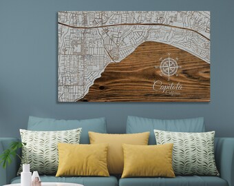 May include: A wooden wall art piece featuring a white engraved map of Capitola, California, with a compass rose and the city name below. The map is on a brown wood background.