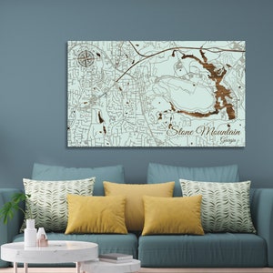 May include: A wooden map of Stone Mountain, Georgia, with a detailed depiction of the city's layout, including roads, buildings, and a compass rose. The map is in shades of brown and light blue, with the text "Stone Mountain, Georgia" displayed prominently.