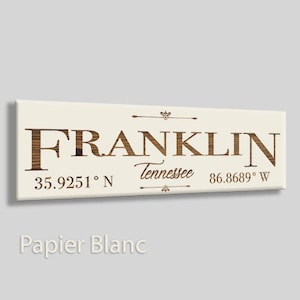 May include: A rectangular canvas print with the word "FRANKLIN" in a wood-grain font. Below, it reads "Tennessee" and coordinates 35.9251° N 86.8689° W. The background is off-white, with decorative flourishes.