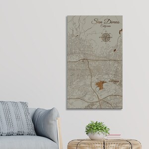 May include: A wood-mounted map of San Dimas, California, with a compass rose in the upper right corner. The map is in a light brown color with a beige background.
