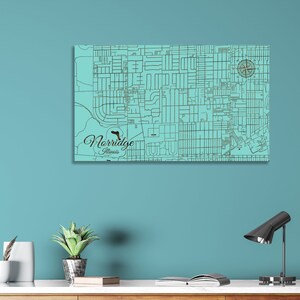May include: A teal blue wooden map of Norridge, Illinois, with black lines representing streets. The map is mounted on a wall with a compass in the upper right corner. The text "Norridge, Illinois" is written in a cursive font in the lower left corner.