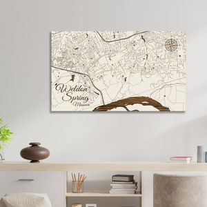 May include: A wooden map of Weldon Spring, Missouri, with a compass rose in the upper right corner. The map is on a white background and has a brown wood grain texture.