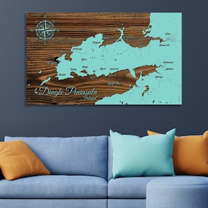 May include: A wooden map of the Dingle Peninsula in Ireland with a light blue outline and the names of towns and cities printed in white. The map is on a brown wooden background with a compass rose in the top left corner.