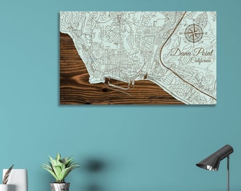 May include: A wooden map of Dana Point, California, with a compass rose and the city name in a decorative font. The map is on a light blue background.