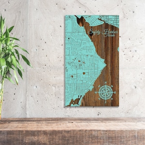 May include: A wooden map of Safety Harbor, Florida, with a compass rose in the bottom right corner. The map is painted in a light blue color and has a brown wood grain background.