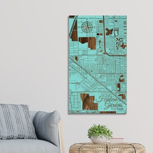 May include: A teal blue wood-mounted map of Hialeah Gardens, Florida. The map features a compass rose and the city name in a cursive font.