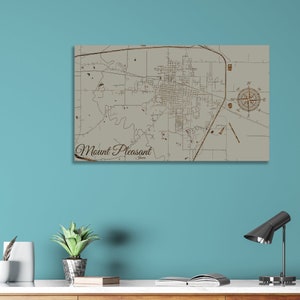 May include: A wood-mounted map of Mount Pleasant, Iowa, with a compass rose in the upper right corner. The map is printed on a light beige background with brown lines and text. The text "Mount Pleasant, Iowa" is printed in a brown cursive font at the bottom of the map.