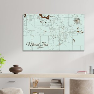 May include: A light blue wooden map of Mount Zion, Illinois, with brown lines representing roads and a compass in the top right corner. The text "Mount Zion, Illinois" is written in brown cursive at the bottom of the map.