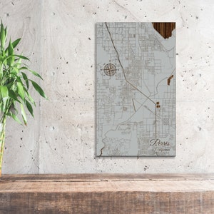 May include: A wood map of Perris, California, with a compass rose and a gray background. The map is mounted on a white wall.