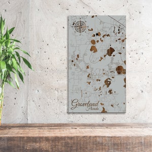 May include: A wood map art piece of Groveland, Florida. The map is laser cut and features a compass rose and the city name.