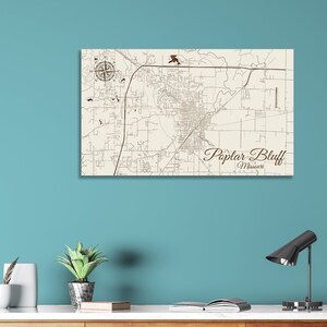 May include: A wood map of Poplar Bluff, Missouri, with a compass rose in the top left corner. The map is on a cream-colored background with brown lines and text.