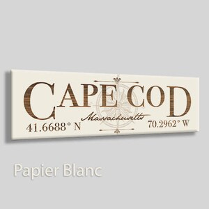 May include: A white sign with brown text that reads "CAPE COD" with a compass graphic and the coordinates "41.6688° N 70.2962° W" and the text "Massachusetts" underneath.