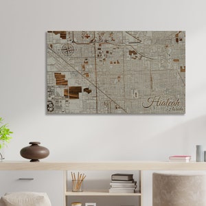 May include: A wood-mounted map of Hialeah, Florida, with a beige background and brown wood accents. The map shows the city's streets and landmarks. The city name is written in cursive at the bottom right corner.