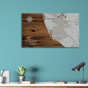 May include: A wood-grain print canvas with a white map of Oxnard, California. The map is centered on the right side of the canvas. The left side of the canvas has a wood grain pattern with a compass rose and the text "Oxnard, California".