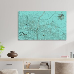 May include: A teal blue map of Brea, California with a compass rose in the top right corner. The city name is written in a brown cursive font at the bottom left corner.