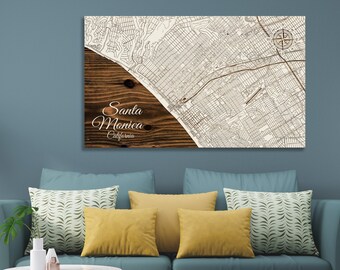May include: A wood-mounted map print of Santa Monica, California. The map is in black and white and shows the streets and landmarks of the city. The wood is a dark brown color and has a natural grain pattern. The text "Santa Monica, California" is printed in white on the wood.
