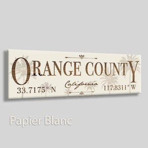 May include: A beige canvas print with a brown wooden design featuring the text "ORANGE COUNTY, California" with the coordinates "33.7175° N 117.8311° W" and palm trees.