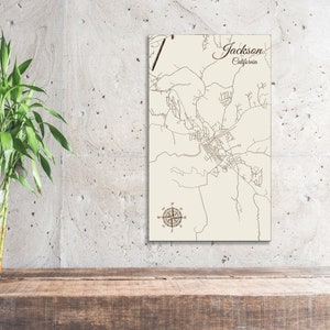 May include: A beige wooden map of Jackson, California, with a compass rose in the bottom center. The map is mounted on a wall.