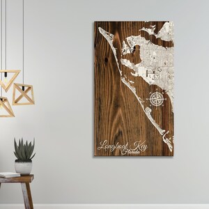 May include: A wood sign with a white outline of Longboat Key, Florida. The sign has a compass rose and the text "Longboat Key Florida" in white cursive.