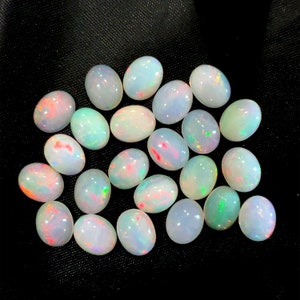 Könnte beinhalten: Eine Sammlung ovaler weißer Opale mit schillernden Regenbogen-Blitzen. Die Opale sind lose und bereit, in Schmuck eingefasst zu werden.