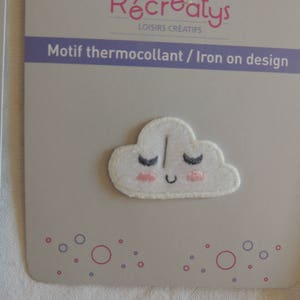 Puede incluir: Parche termoadhesivo blanco con un diseño de nube sonriente. La nube tiene mejillas rosadas y ojos cerrados con pestañas. El texto "Motif thermocollant / Iron on design" está impreso en el embalaje.