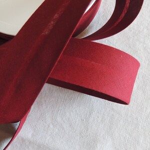 Peut inclure: Un rouleau de biais rouge foncé, un type de garniture en tissu utilisé pour la finition des bords des vêtements et des projets de décoration intérieure.