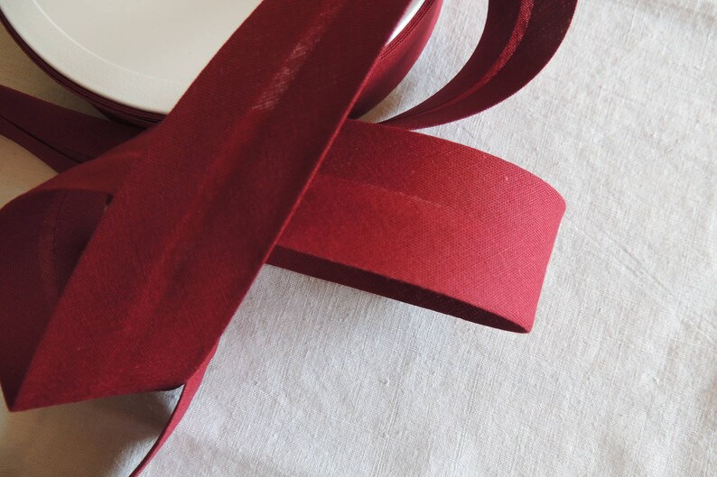 May include: A roll of deep red bias binding, a type of fabric trim used for finishing edges of garments and home decor projects.