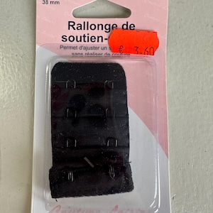 Pode incluir: Extensor de sutiã preto com três fechos de colchete, embalado em um cartão rosa e branco. O cartão diz "2 Crochets 38 mm" e "Rallonge de soutien-". Permite ajustar um sutiã sem costurar.