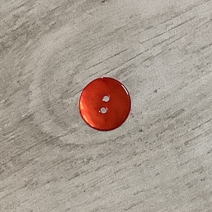 May include: A bright orange plastic button with two holes.