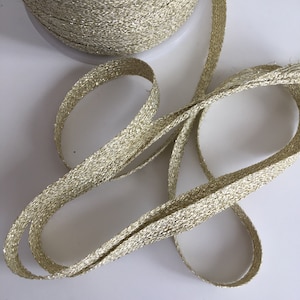 Può includere: Un rotolo di nastro dorato con glitter. Il nastro è intrecciato con un motivo testurizzato e ha un leggero luccichio.