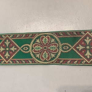 Puede incluir: Borde verde, rojo y dorado con un patrón repetido de flores y diamantes estilizados. El borde está tejido con una textura en relieve.