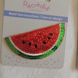 Può includere: Un toppa termoadesiva a forma di anguria rossa e verde con paillettes. La toppa è su una carta bianca con il testo "Récréatys Loisirs Créatifs Motif thermocollant / Iron on design" stampato su di essa.