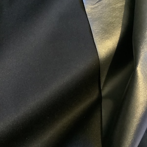 Peut inclure: Gros plan sur deux échantillons de tissu. L'un est un tissu noir foncé à la texture lisse. L'autre est un tissu argenté avec un léger brillant.