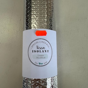 Könnte beinhalten: Eine aufgerollte, silberfarbene Isolierfolie, beschriftet mit "Special Lunch Box Tissu Isolant". Das Etikett weist eine Gutscheingröße von 70 x 100 cm aus. Das Gewebe dient dazu, Lebensmittel stabil zu temperieren.
