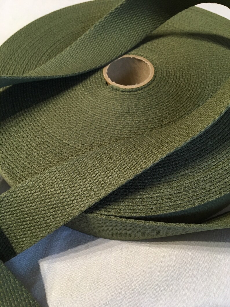 May include: A roll of olive green cotton webbing, a type of heavy-duty fabric used for straps and belts.