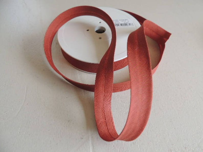 Pode incluir: Uma bobina de fita de vi&eacute;s cor de ferrugem, um tipo de acabamento de tecido usado para finalizar as bordas de roupas e projetos de decora&ccedil;&atilde;o de casa.