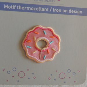 Peut inclure: Patch thermocollant en forme de donut rose avec des pépites colorées. Le patch est sur une carte blanche avec le texte "Motif thermocollant / Iron on design".