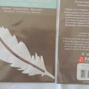 Peut inclure: Un patch thermocollant blanc en forme de plume. Le patch est sur une carte brune avec des instructions pour appliquer le patch sur du tissu. Les instructions sont en anglais et en français. La carte comprend également le nom de la marque "Paritys" et le numéro de référence du produit "3793".