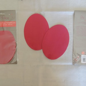 Peut inclure: Deux patchs thermocollants rouges pour réparer les vêtements. Les patchs sont ronds et ont une surface lisse. L'emballage comprend le texte "Pic & Malice" et "1 paire de coutures/re-patches/THERMOCOLLANT".