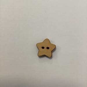 Può includere: Un bottone di legno a forma di stella con due fori neri. Il bottone è marrone chiaro con un bordo marrone più scuro. Questo materiale artigianale è ideale per cucire, fare scrapbooking o altri progetti fai-da-te.
