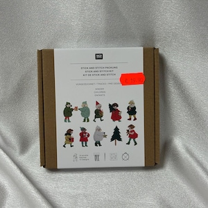 Puede incluir: Una caja de cartón marrón con una etiqueta blanca con texto en varios idiomas, incluyendo "STICK AND STITCH PACKUNG" y "CHILDREN". La caja muestra varios diseños de parches bordados de personajes festivos y un árbol de Navidad.