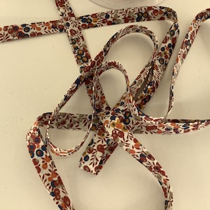 Op de afbeelding: Een wit lint met een bloemenpatroon in tinten rood, oranje, blauw en groen. Het lint is gemaakt van katoen en heeft een subtiele glans.