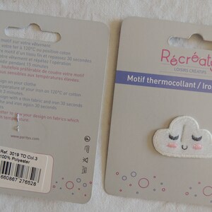 May include: A white iron-on patch featuring a smiling cloud design. The patch has pink cheeks and black eyelashes. The packaging includes instructions for applying the patch to fabric. The text on the packaging reads "R&eacute;cr&eacute;atys Loisirs Cr&eacute;atifs Motif thermocollant / Iron on design".