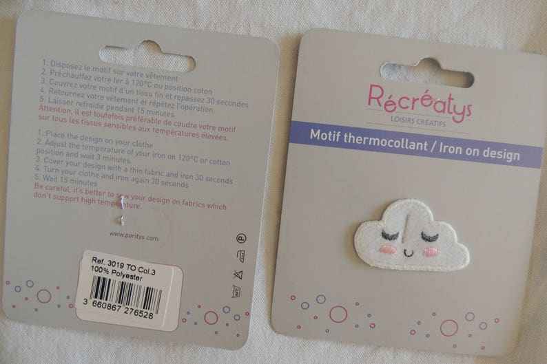 May include: A white iron-on patch featuring a smiling cloud design. The patch has pink cheeks and black eyelashes. The packaging includes instructions for applying the patch to fabric. The text on the packaging reads "R&eacute;cr&eacute;atys Loisirs Cr&eacute;atifs Motif thermocollant / Iron on design".