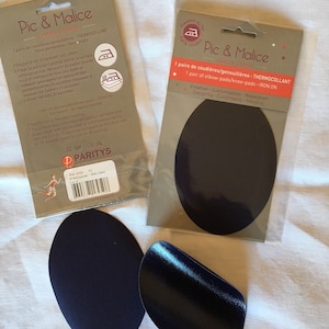 May include: Two packages of iron-on elbow or knee pads. The packages are white with black text and images. The pads are dark blue and oval shaped. The text on the packages reads "Pic & Malice Couture créative 1 paire de coudières/genouillères - THERMOCOLLANT 1 pair of elbow-pads/knee-pads - IRON ON"
