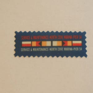 Könnte beinhalten: Ein blauer und weißer Aufkleber mit dem Text "SERVICE & MAINTENANCE NORTH COVE MARINA PIER 54" und einer Reihe von fünf bunten Flaggen.