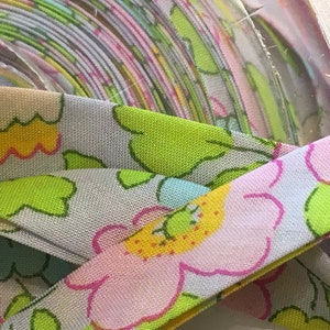 Peut inclure: Un rouleau de tissu bleu clair avec un imprimé floral rose, jaune et vert. Le tissu est plié et enroulé, et le motif floral est visible sur l'extérieur du rouleau.